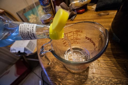 Pouring vinegar into a glass measuring cup, before adding sugar and salt.